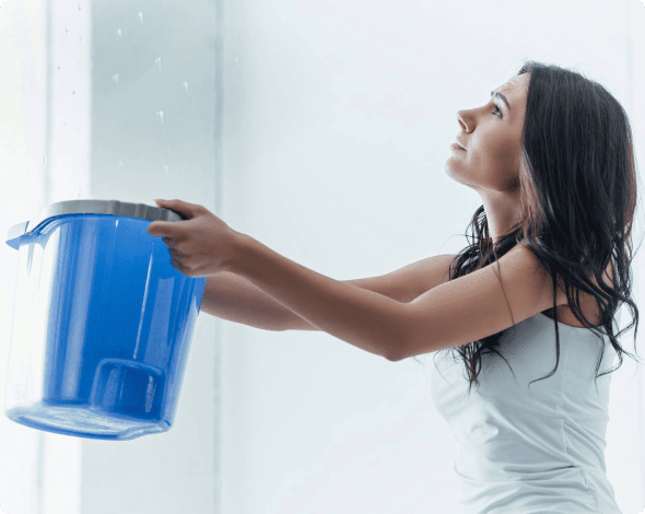 Image of a woman holding a bucket under a bathroom ceiling leak.