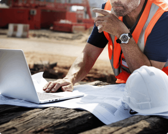 A contractor on-site looking at blueprints and a laptop.