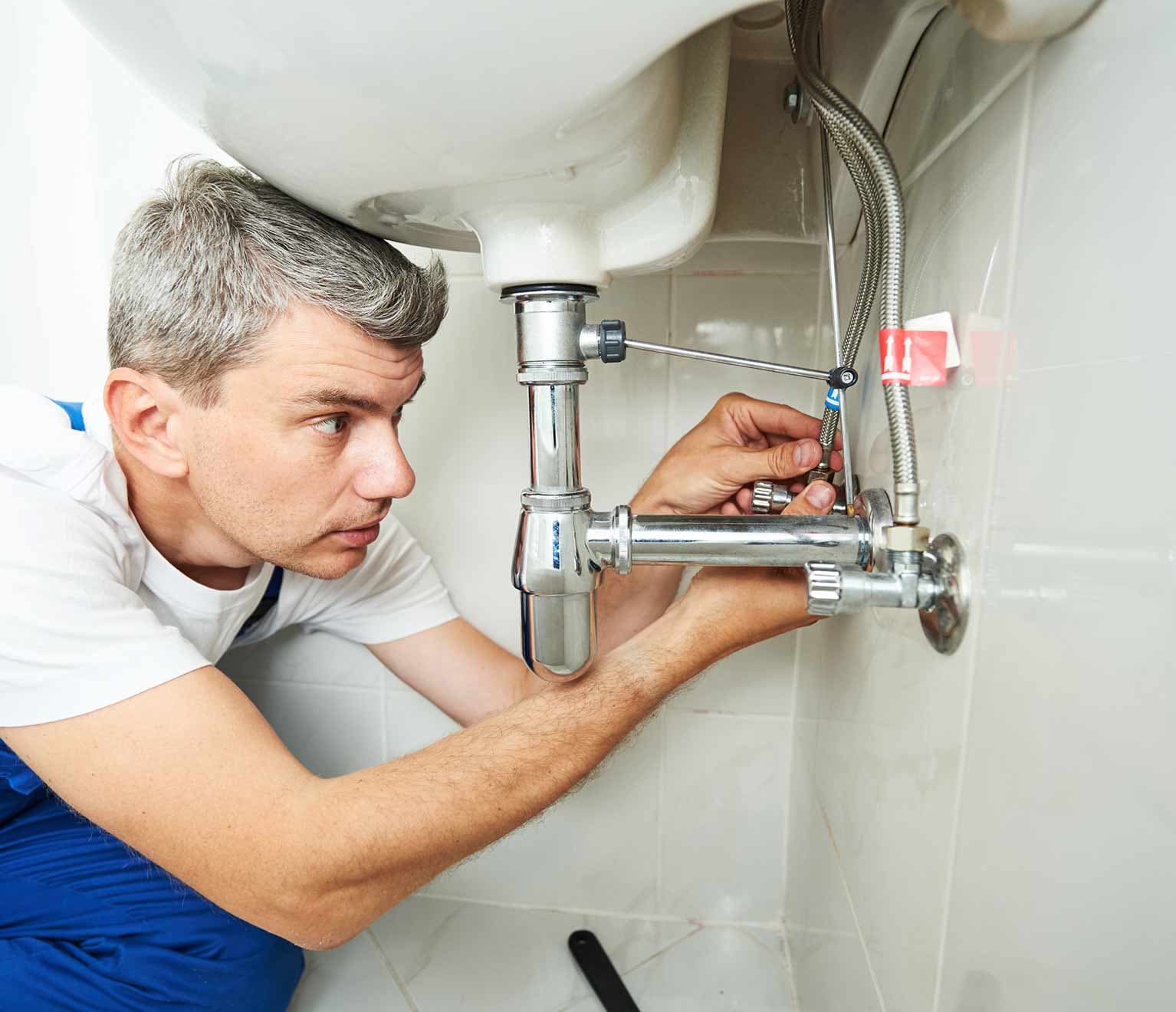 Image of a homeowner making repairs to plumbing under the sink.