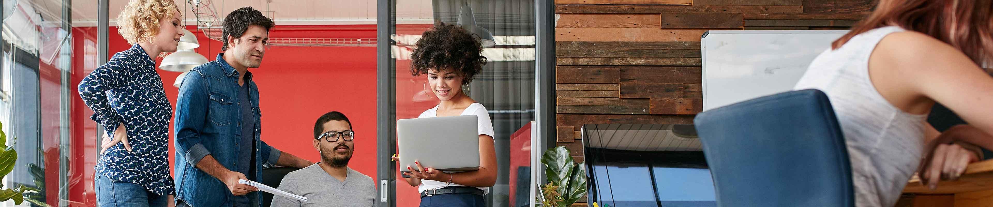 A group of coworkers looking at a laptop in a modern office.