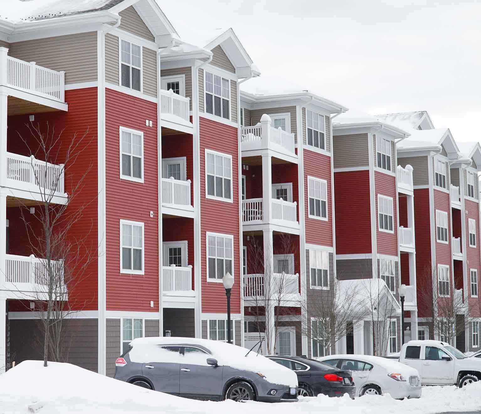 Red and tan apartment complex in winter with snow on roof.