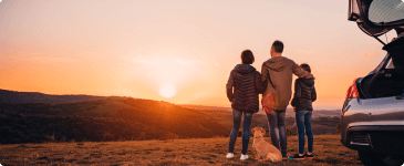 a family of three looking at the sunset by their parked car