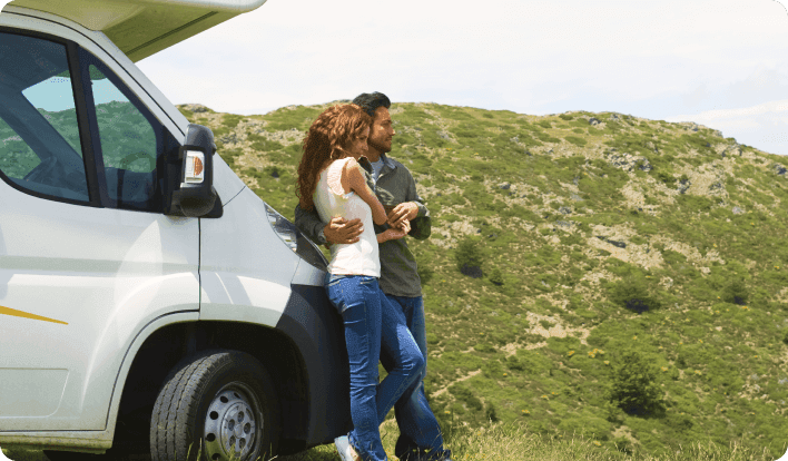 a man and woman holding each other and leaning against an RV